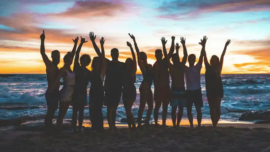 A group of friends raising their arms on the beach at sunset